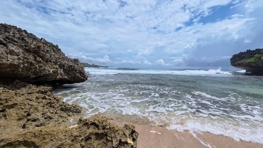 Ocean waves crashing against sharp coral rocks at Mbuluk Beach, Gunung Kidul, Yogyakarta, Indonesia