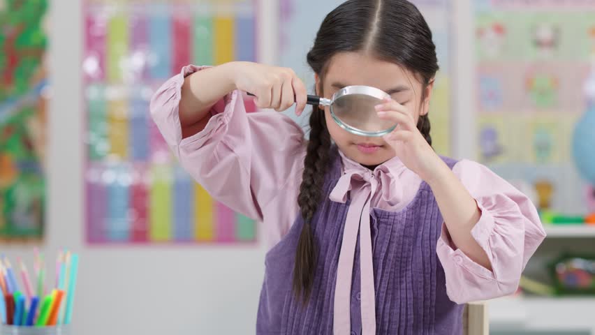 Young girl with braids inspects closely using magnifying glass in bright, colorful classroom setting
