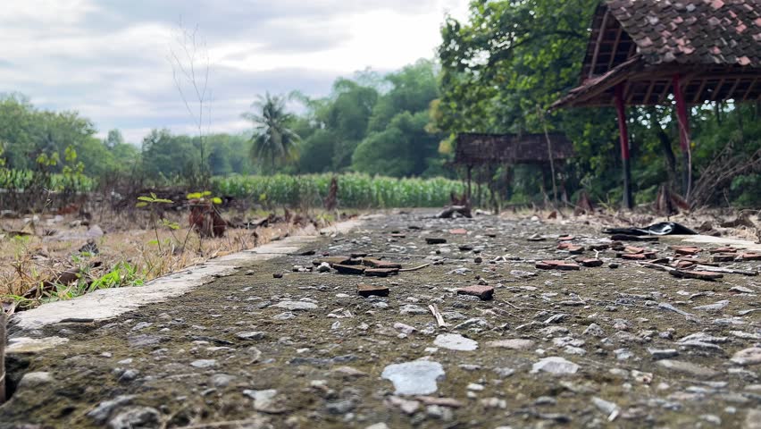 Abandoned rural road with scattered rubble near old wooden structure, depicting neglect and countryside decay.