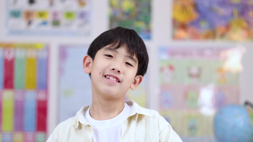 Smiling young Asian student holds a yellow number eight cutout in a bright classroom