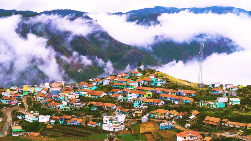 Aerial view of a beautiful mountain village in Kodaikanal, India, featuring misty white clouds, lush green hills, charming rooftops, and scenic valleys, highlighting a popular tourist attraction and serene hill station landscape under soft daylight. 12 November 2024