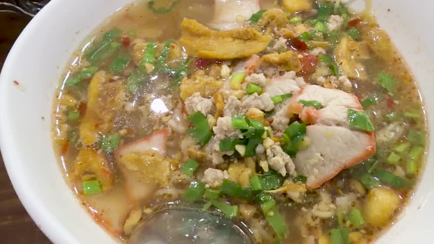 Close-up shot of chopsticks lifting egg noodles from a spicy pork broth bowl