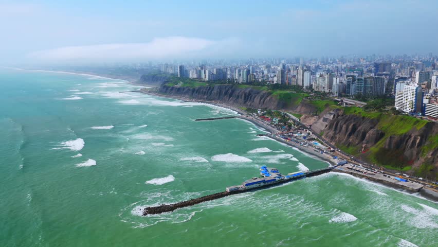 Sunny morning Miraflores Barranco Barranquito Playa Makaha beach pier aerial drone Lima Peru clear hazy blue skies residential skyscraper buildings cars traffic highway ocean view surf waves static