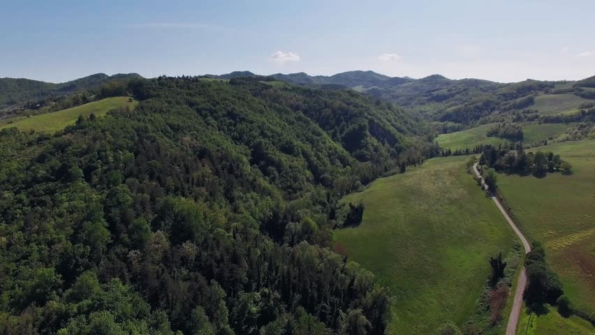 Drone footage of lush green hills and forested valleys under a sunny sky, showcasing a vibrant rural landscape.