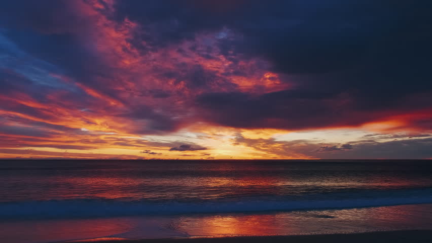 Beach landscape after sunset with vibrant red and orange sky reflecting on water and shore. Beautiful seascape time lapse, 4k