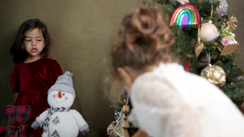 A happy young girl in a red dress laughs while holding a plush snowman next to a decorated Christmas tree
