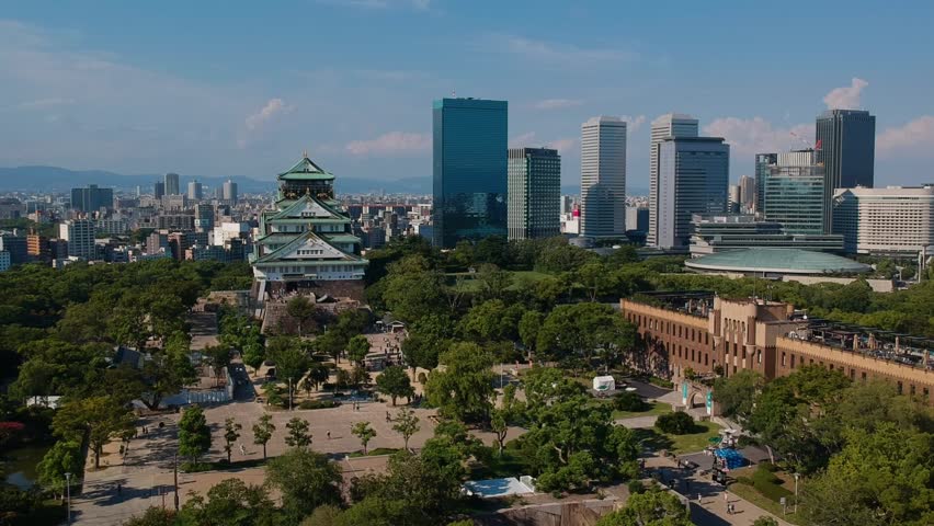 Aerial drone shot moving forward toward Osaka Castle with modern city skyline.