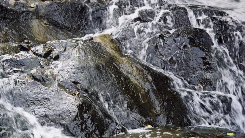 Water flowing over textured rocks in a natural stream creating steady motion and detail.
