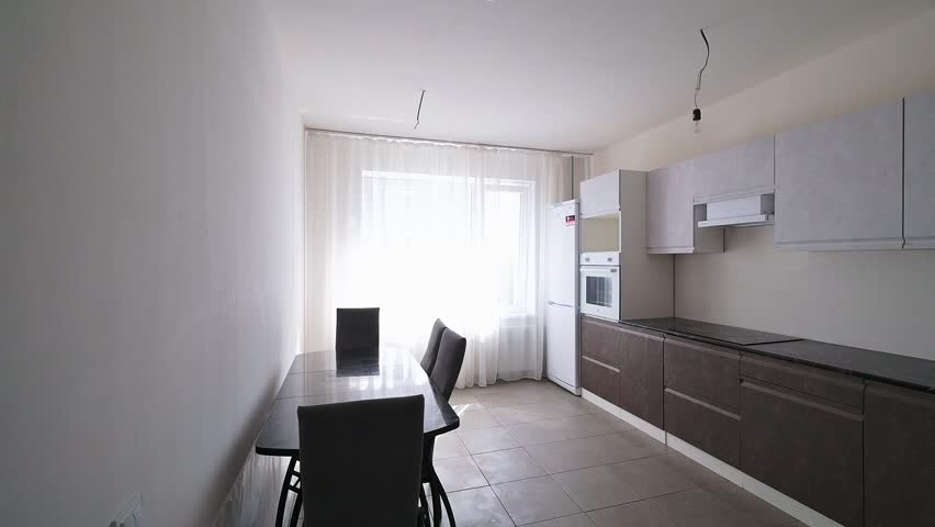 minimalist kitchen with dark lower cabinets, white upper cabinets, a glass dining table, black chairs, sheer curtains, and a white refrigerator; clean, bright space with tiled flooring