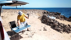 Content creator recording a video with a smartphone gimbal on a beach, working remotely with his laptop from the trunk of a van. This freelancer is enjoying the freedom of a nomadic lifestyle - Powered by Shutterstock - Get 15% off with code: PIKWIZARD15