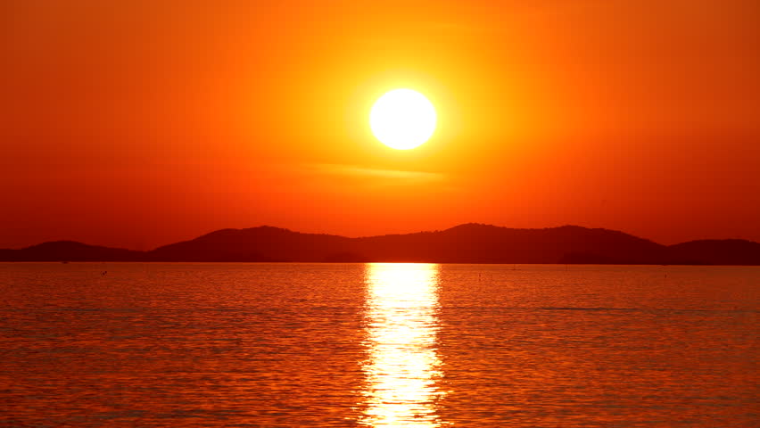 Time-lapse of a large round sun setting slowly over the calm sea at the horizon