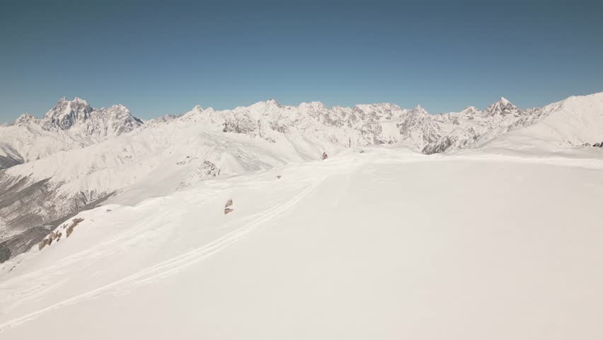 Drone aerial view of untouched snowy Caucasus mountains in winter with clear skies, panoramic ridgelines, and frozen alpine landscape