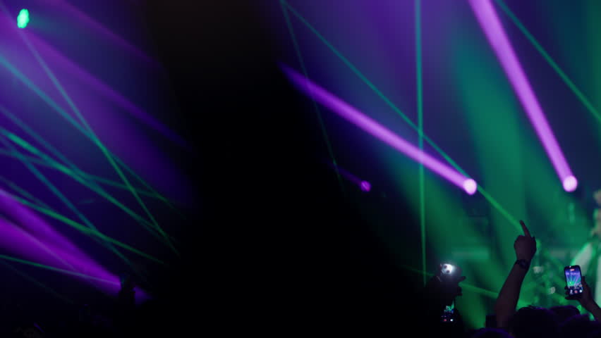 Bright green and purple laser light show fills concert space above dancing crowd creating immersive club atmosphere