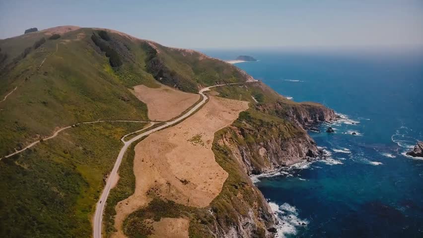 Cinematic aerial view of Highway 1 along the Pacific Ocean in Big Sur, California, capturing summer scenery, cliffs, and stunning coastal vistas.