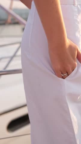 A fashionable young woman wearing a striped top, white pants, a red scarf, and chic sunglasses relaxes on a boat. She enjoys the sunny weather, embodying a serene and stylish summer vacation lifestyle.