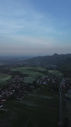 Aerial drone footage showing a rural valley landscape with farmland, agricultural fields, and a small village during blue hour. The wide aerial perspective reveals patterns of fields, village rooftops, and surrounding hills as soft evening light spreads across the countryside. Subtle blue tones in the sky and gentle shadows create a calm and tranquil atmosphere.
This scenic rural footage is ideal for projects related to countryside life, agriculture, travel, environment, and outdoor scenery. The combination of open farmland, valley terrain, and rural settlement makes it suitable for documentaries, cinematic videos, commercials, presentations, and background visuals. The peaceful mood and wide composition help convey themes of rural living, simplicity, harmony with nature, and slow-paced lifestyle.
With no visible people, text, or logos, this video offers flexible commercial use for media, education, tourism promotion, and creative storytelling.
