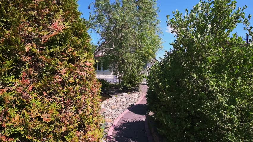 serene suburban house surrounded by lush greenery, featuring a decorative stone pathway, a tranquil pond with rocks, and a charming metal bridge