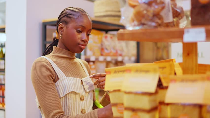 Thoughtful young woman carefully reading the ingredients on a product package. Customer choosing healthy food in a grocery store
