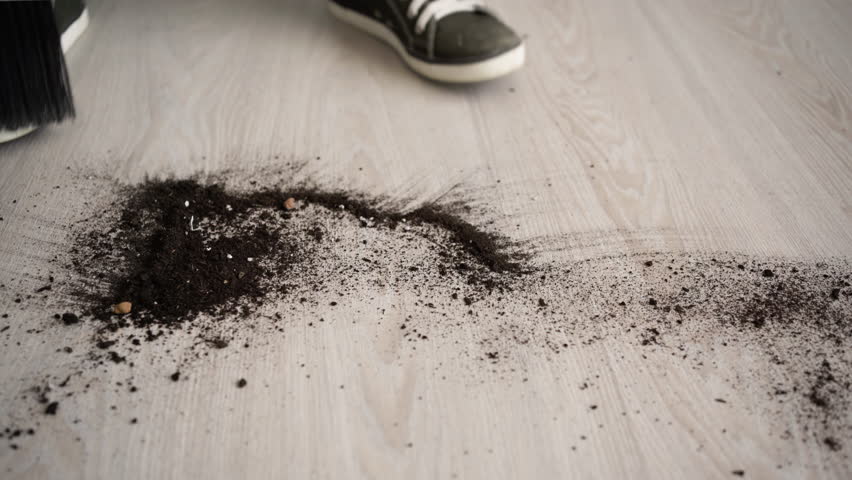 Close up of a person sweeping spilled soil from the floor with a broom and dustpan.