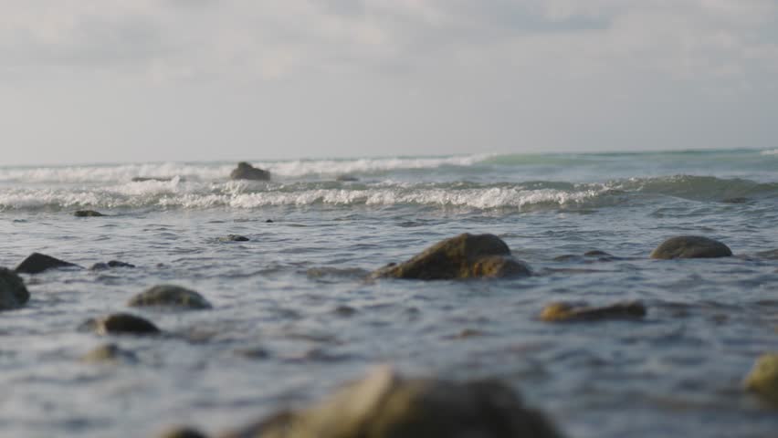 Slow motion ocean wave gently washing over small rocks