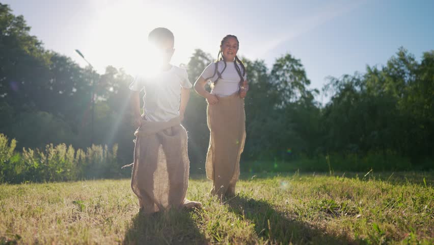 Two children field. Children race in the grass outdoors with sack of sunlight. Young girl is playing with a teddy bear in nature during a fun competition in summer. A pair of kids in a lifestyle.