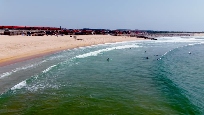 Aerial establishing shot of surfers in ocean near sandy beach coastline. Espinho, Portugal 