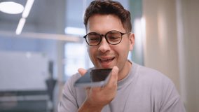 Young man holding smartphone close to mouth while recording voice message, modern bright interior with soft daylight showing mobile communication, technology and casual daily interaction - Powered by Shutterstock - Get 15% off with code: PIKWIZARD15