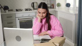 Woman sits at laptop in room, surrounded by educational books, taking notes, flipping through notes. Businesswoman or student at laptop watches online webinar or training course. Online e-learning. - Powered by Shutterstock - Get 15% off with code: PIKWIZARD15