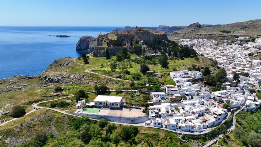Aerial drone cinematic video of archaeological site of Acropolis of Lindos vilage featuring amazing organized beach and iconic Saint Paul bay, Rhodes island, Dodecanese, Greece