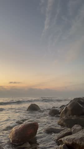 Vertical video of ocean waves washing over rocks on a natural beach. Calm coastal seascape suitable for background, wellness, meditation and design projects.