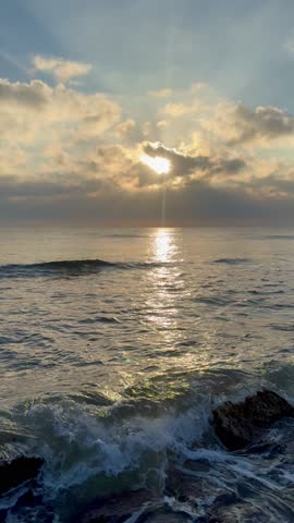 Vertical video of ocean waves washing over rocks on a natural beach. Calm coastal seascape suitable for background, wellness, meditation and design projects.