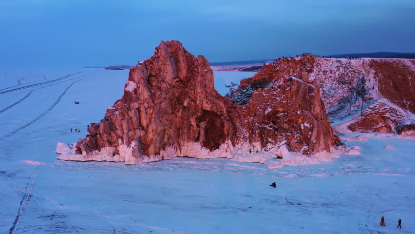 Aerial around view of Shaman rock at sunset, one of sacred place in frozen lake Baikal in winter season of Siberia, Russia, 4k