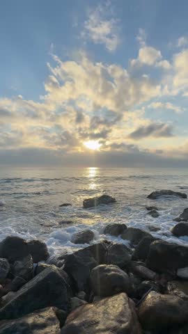 Vertical video of ocean waves washing over rocks on a natural beach. Calm coastal seascape suitable for background, wellness, meditation and design projects.