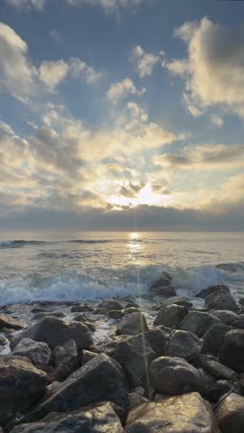 Vertical video of ocean waves washing over rocks on a natural beach. Calm coastal seascape suitable for background, wellness, meditation and design projects.