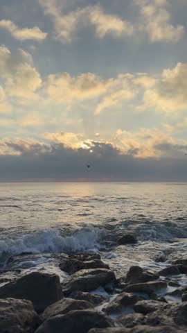 Vertical video of ocean waves washing over rocks on a natural beach. Calm coastal seascape suitable for background, wellness, meditation and design projects.