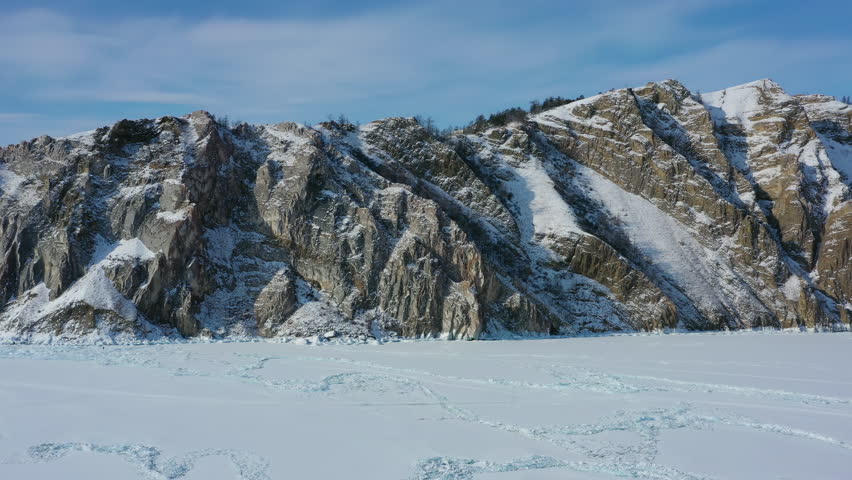 Aerial around view of Rocky shore of Olkhon Island on frozen Lake Baikal. Siberia, Russia, 4k