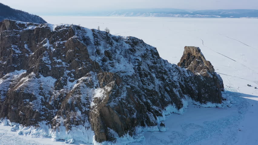 Aerial around view of frozen Lake Baikal, Olkhon Island, Khoboy rock cape. Siberia, Russia, 4k