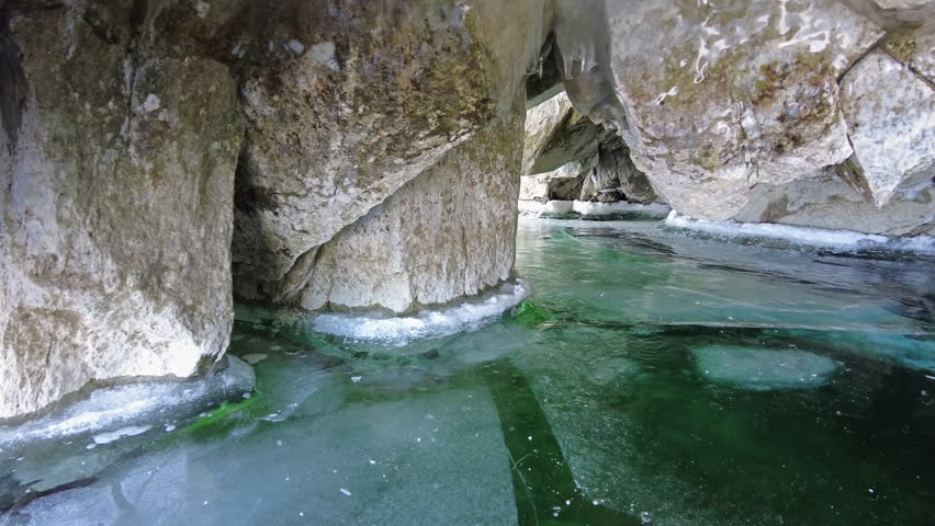 Ice cave on Baikal lake in winter. Clear transparent ice and icicles in grotto. Olkhon island, Baikal, Siberia, Russia, panorama 4k