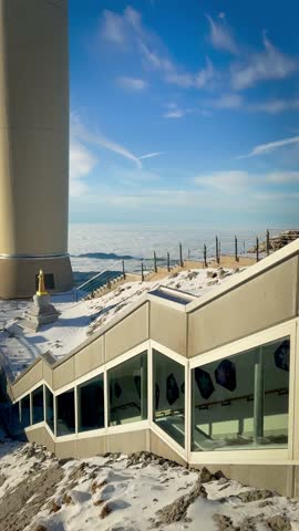 Cinematic winter view of the Säntis summit station in the Swiss Alps. Modern architecture and observation decks overlook a majestic sea of clouds and snow-capped peaks at sunset in Switzerland.