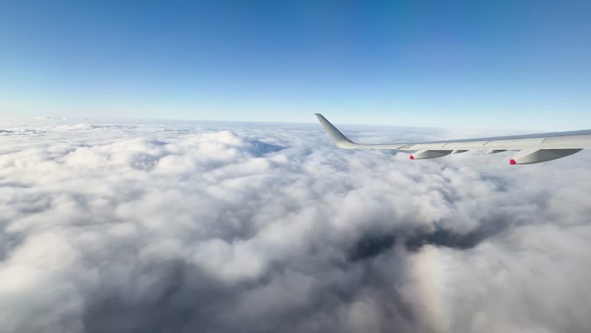 High altitude aerial view of a jet wing flying above a thick cloud deck