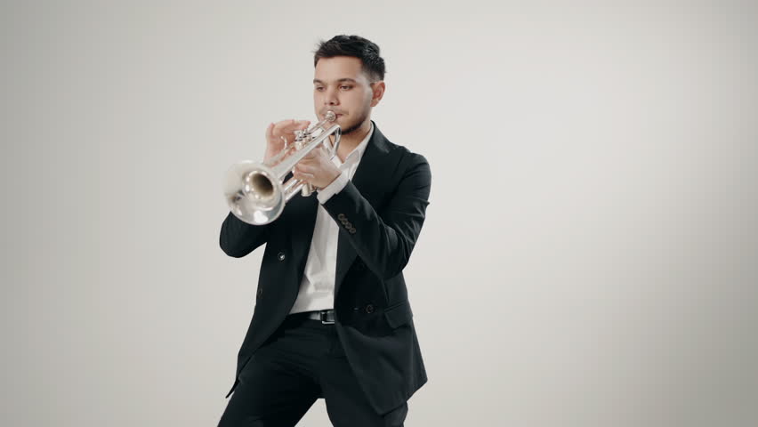 A male jazz singer plays the trumpet on a white background in a modern studio. Playing live jazz concert. Passion for music. Close Up hand of young trumpet player. Music room.