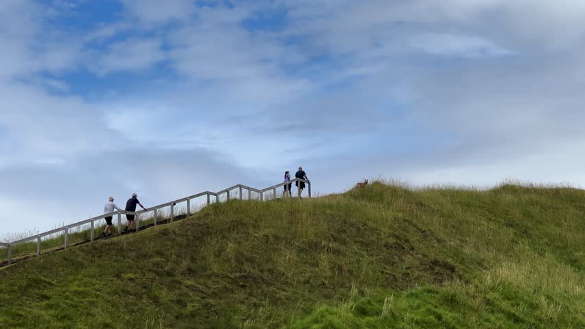 Looking up a wild path to go through uphill on a green grass meadow hill under cloudy skies.
