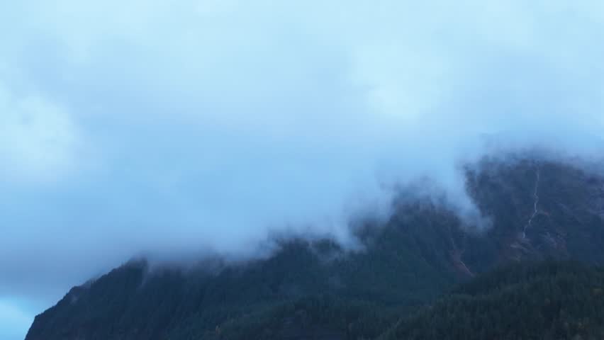 Gimbal wide booming down shot of majestic Mendenhall Glacier and Nugget Falls below misty mountains in Juneau, Alaska. 4K