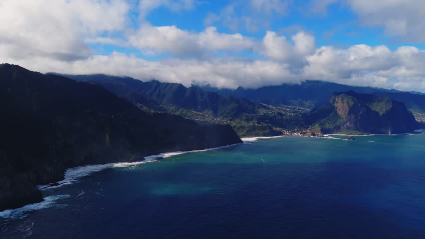 Aerial view of Madeira Island, Portugal, with cliffs, villages, terraced fields, and surf near Funchal and Ponta de Sao Lourenco, midday light and cloud shadows move