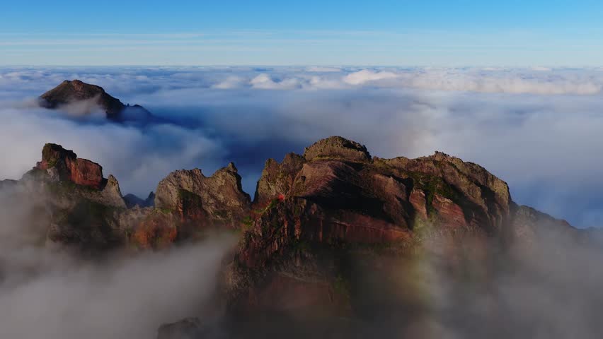 Early morning light casts long shadows on basalt cliffs and evergreen ridges in Madeira Pico do Arieiro, Portugal, as moving cloud banks reveal new summits and a faint mist halo.