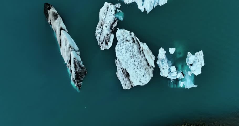 Aerial view of several broken icebergs floating in dark blue glacial water near Vatnajökull, Iceland, showing scattered blocks of ice on calm lagoon water.