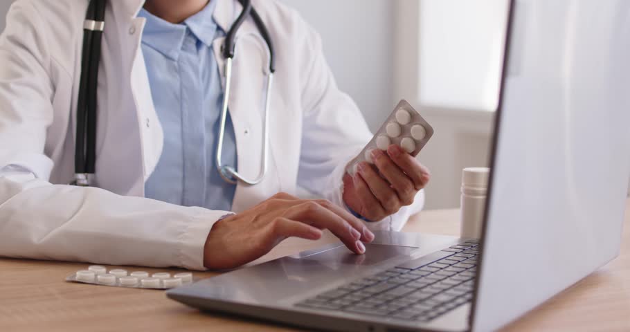 Doctor searches online medicine instruction and dosage. With pills by a laptop, clinician does search for prescription details and side effects on medical sites. Clear guide for safe care.