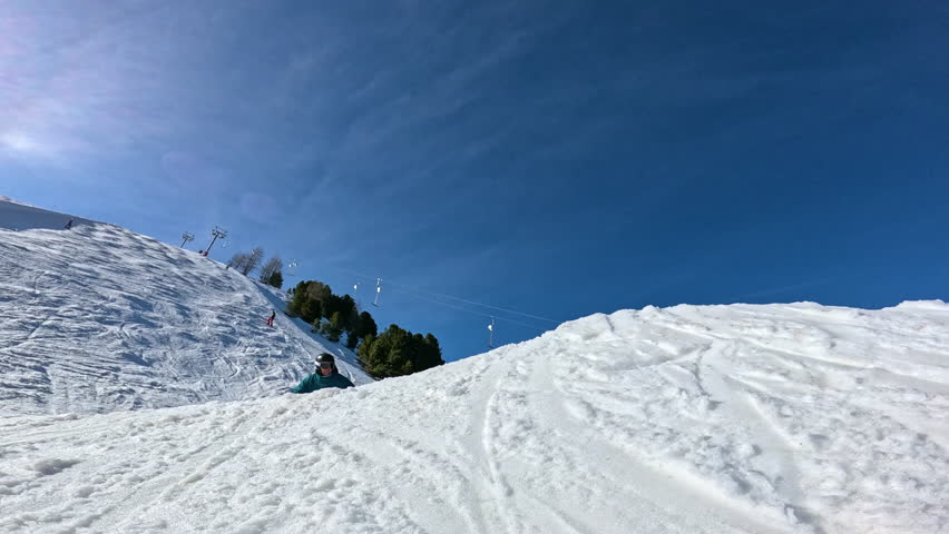 LOW ANGLE VIEW, SLOW MOTION: Male snowboarder in blue jacket makes a melon grab during jump on a fun feature in snowpark. Freestyle rider enjoys doing park laps at sunny ski resort in Austrian Alps.