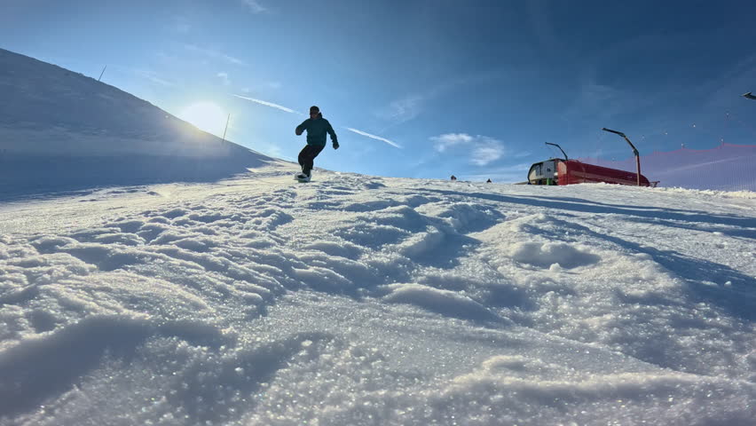 LENS FLARE, CLOSE UP, LOW ANGLE VIEW, SLOW MOTION: Male rider falls forward while snowboarding on ski slope, his hands digging into snow and blasting powder toward camera on sunny winter day in Alps.