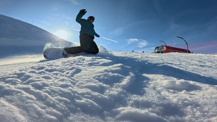 LENS FLARE, CLOSE UP, LOW ANGLE VIEW, SLOW MOTION: Male rider falls forward while snowboarding on ski slope, his hands digging into snow and blasting powder toward camera on sunny winter day in Alps.